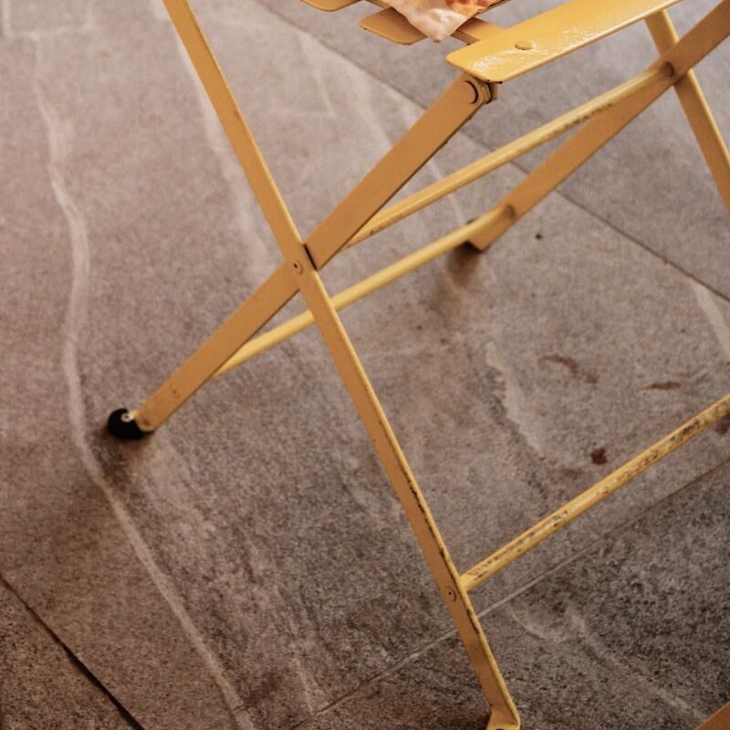 Charming yellow folding chair with a striped cushion on stone flooring, ideal for patios.