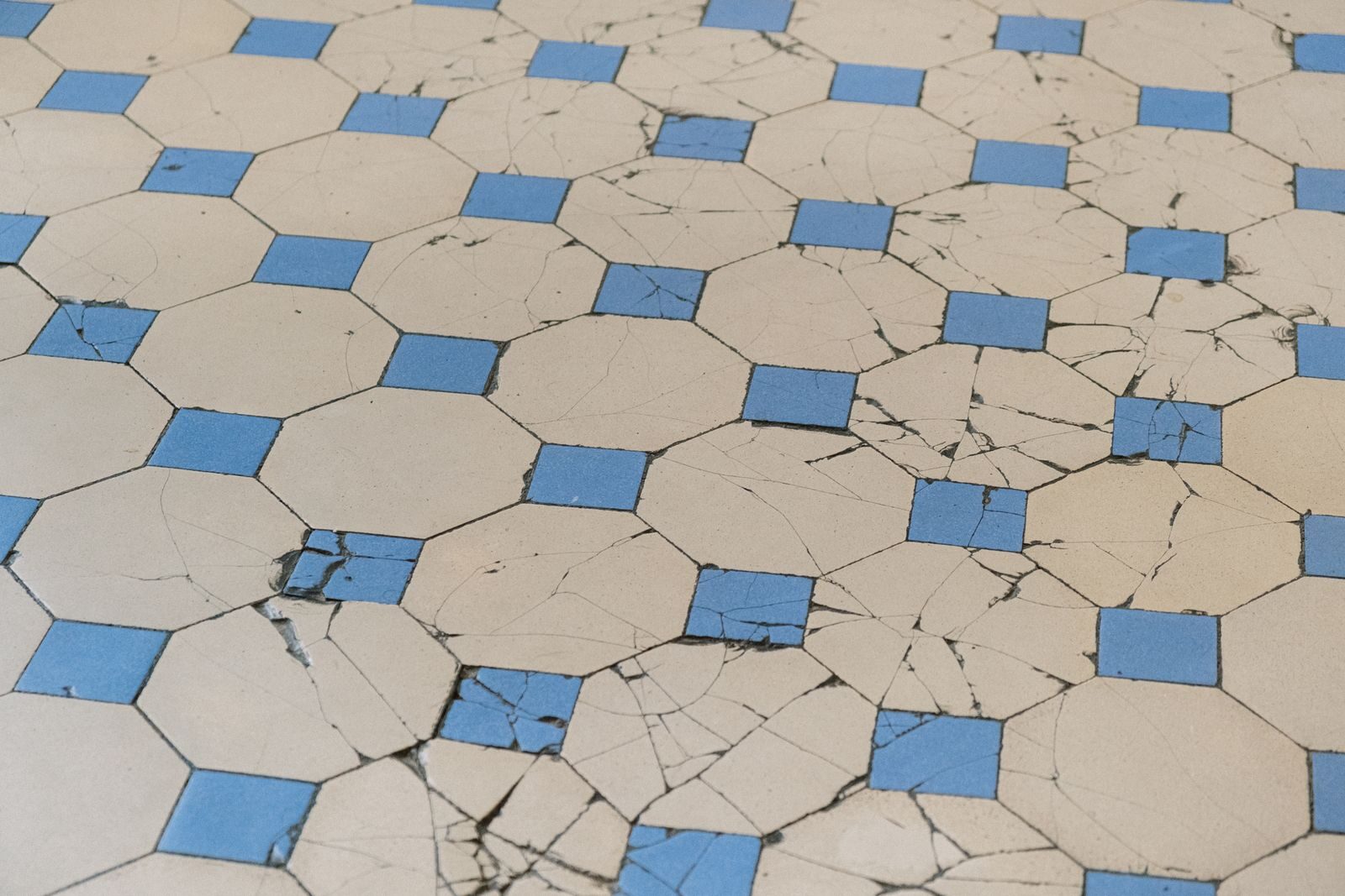 A detailed view of aged cracked tiles with a blue and white geometric pattern.