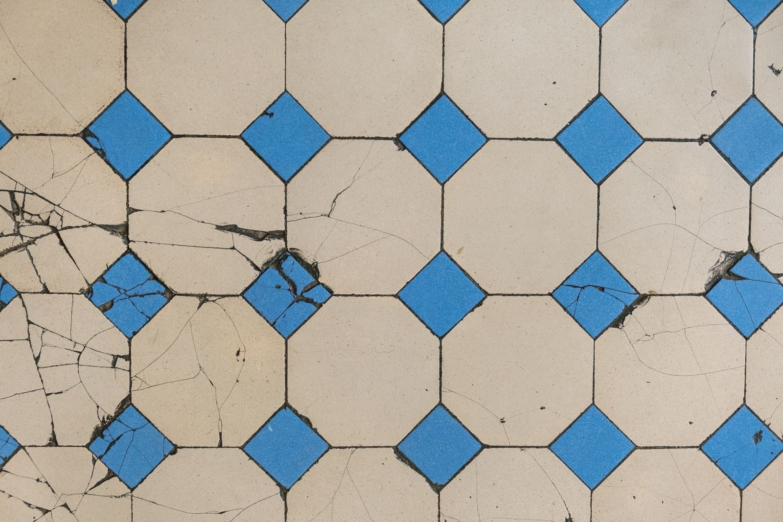 Top view of a cracked geometric tile pattern featuring blue diamond tiles on a beige background.