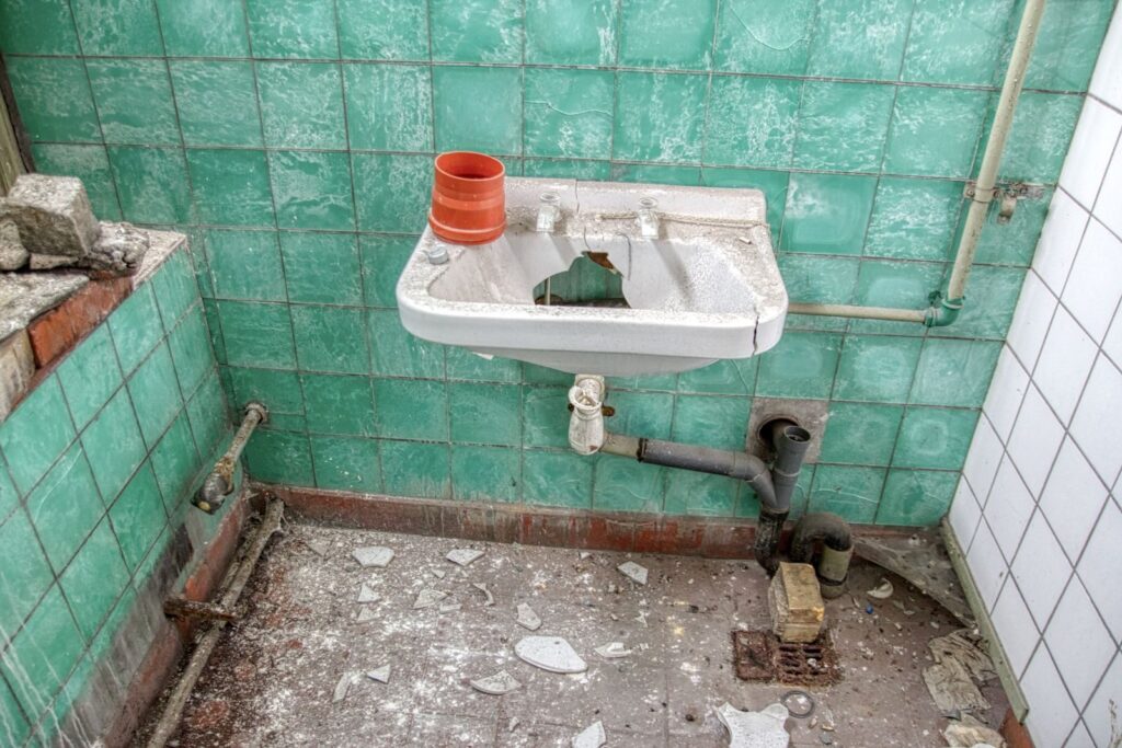 An abandoned bathroom in Leipzig with a shattered sink and peeling tiles.